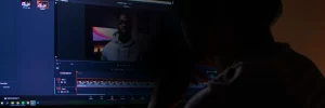 Person sitting in front of a computer screen editing a video, with a paused frame of someone in a hoodie visible in the software—capturing moments that tell the story About Symphonic through every carefully edited scene.