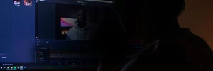 A person sits in front of a computer screen displaying video editing software with footage of a man in a hoodie, possibly working on content about Symphonic.